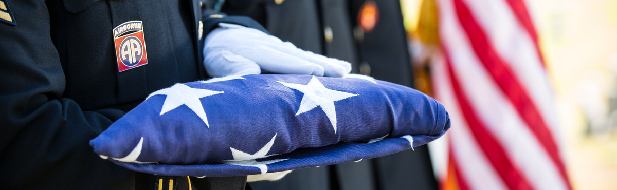 White gloved hands hold a folded American flag.